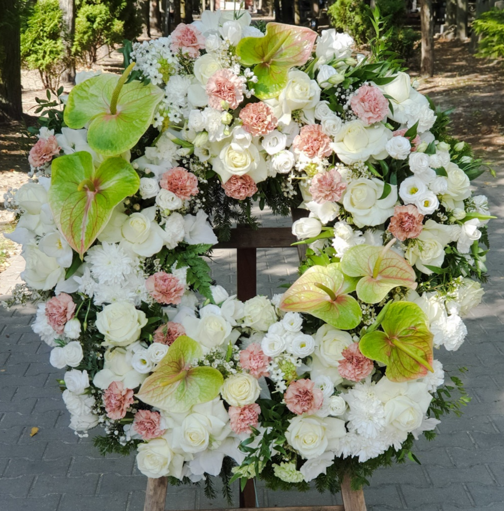 Pastelowy wieniec funeralny z egzotycznych anturium, klasycznych białych róż i goździków. Okrągły wieniec z zielono-różowych anturium, białych róż, kremowych goździków i eustomy.