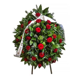 Stojący wieniec pogrzebowy z czerwonych róż na stojaku z białą szarfą.