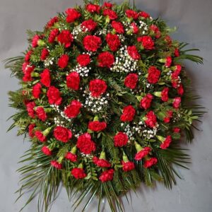 Duży wieniec pogrzebowy z czerwonych goździków, białej gipsówki i gałązek jodły.